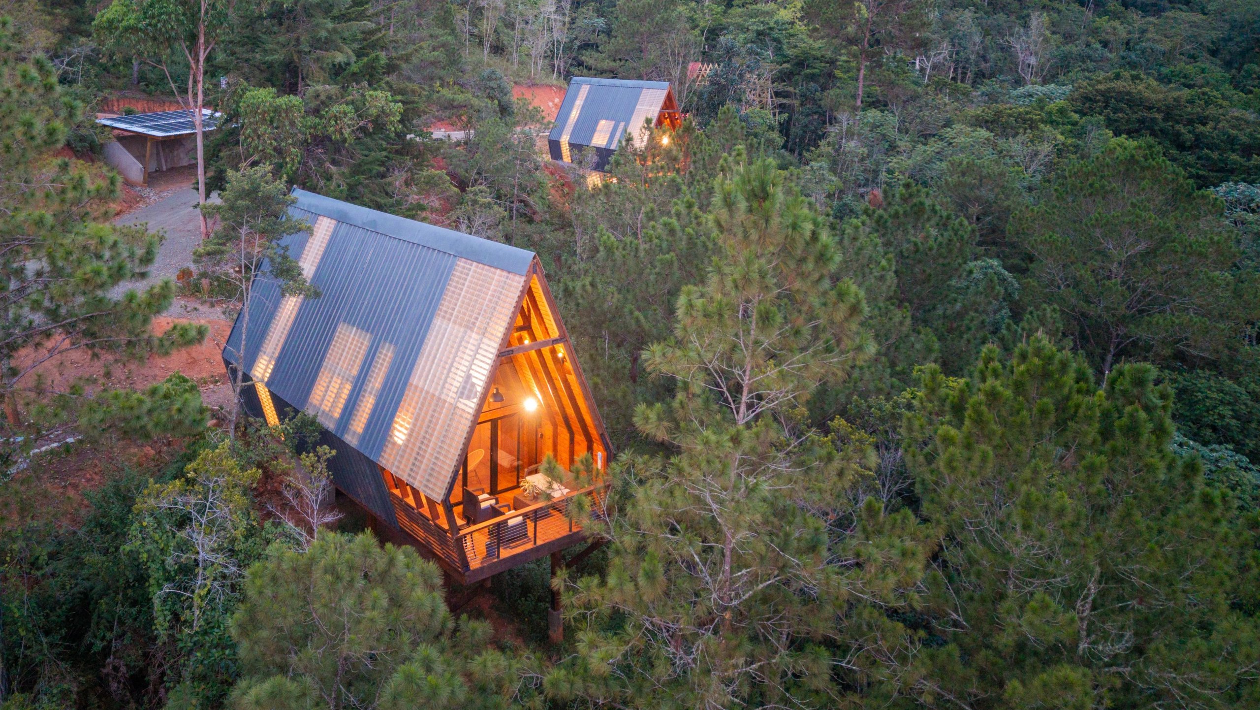Two Estancia Natura A-Frame cabins glowing at dusk within the pine forest